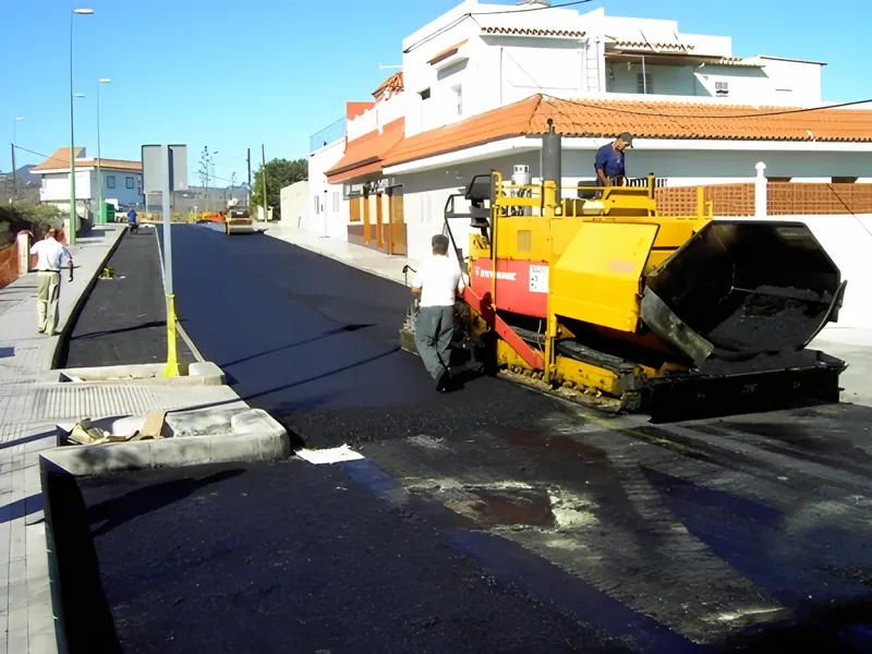 Extendedora de aglomerado y operarios asfaltando una calle